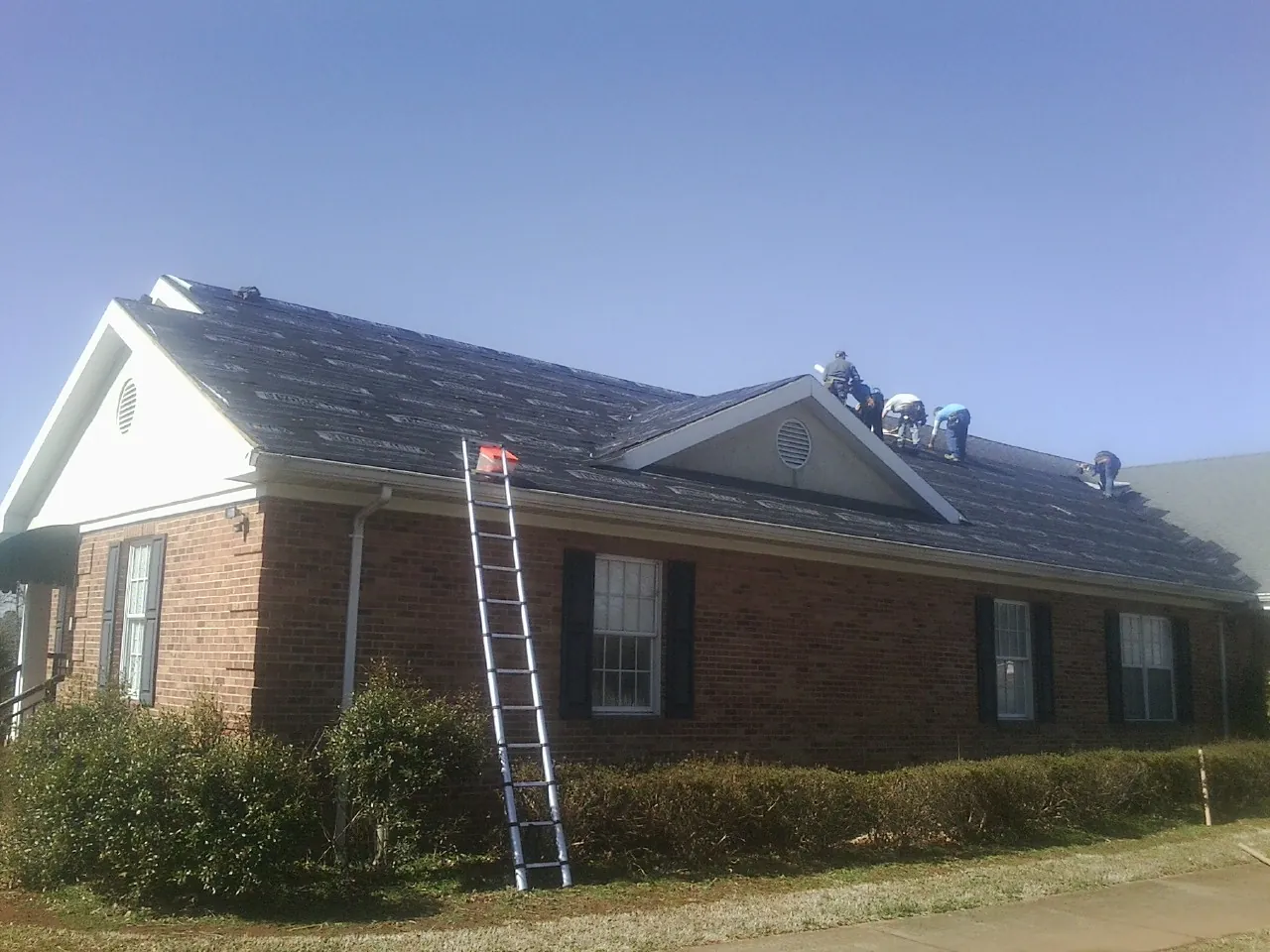Crew tearing shingles off a brick ranch roof with a ladder set — Emergency Roof Repair work by our crew in Cleveland